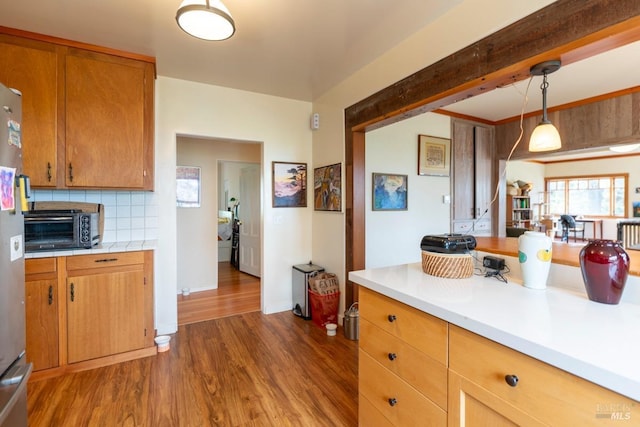 kitchen featuring pendant lighting, decorative backsplash, light countertops, a toaster, and dark wood-type flooring
