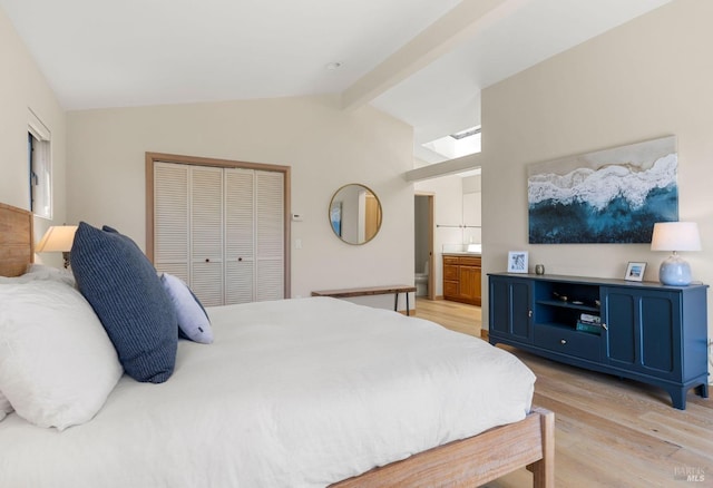 bedroom featuring light wood-type flooring, lofted ceiling with beams, connected bathroom, and a closet
