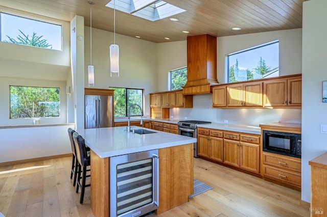 kitchen with a sink, beverage cooler, stainless steel appliances, a towering ceiling, and a skylight