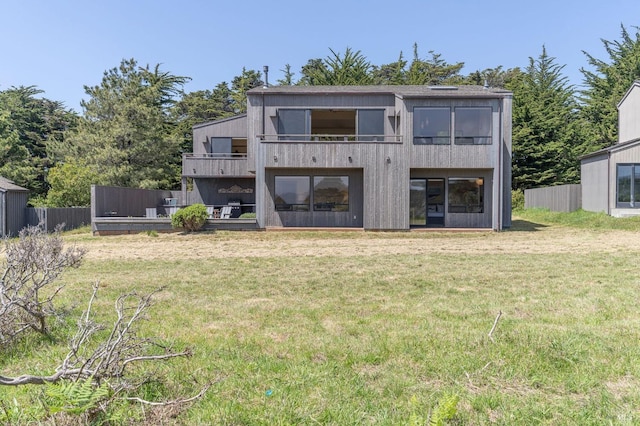 back of property with fence, a yard, and a balcony