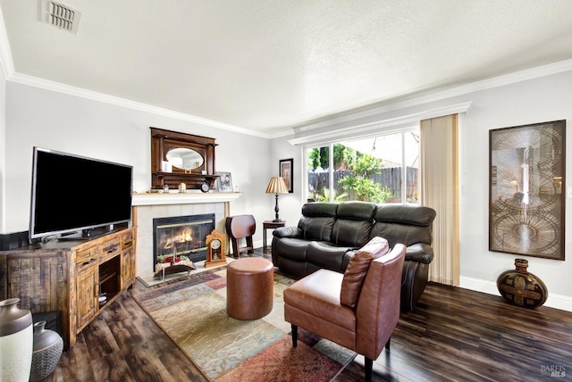 living room featuring a tile fireplace, wood finished floors, visible vents, baseboards, and ornamental molding