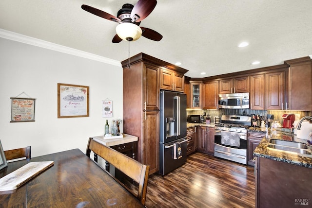 kitchen with ornamental molding, ceiling fan, a sink, dark stone countertops, and stainless steel appliances