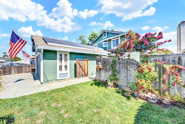 rear view of property with roof mounted solar panels, a yard, an outbuilding, and a fenced backyard