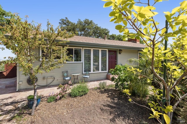 view of front of house featuring a chimney, a patio area, and a shingled roof