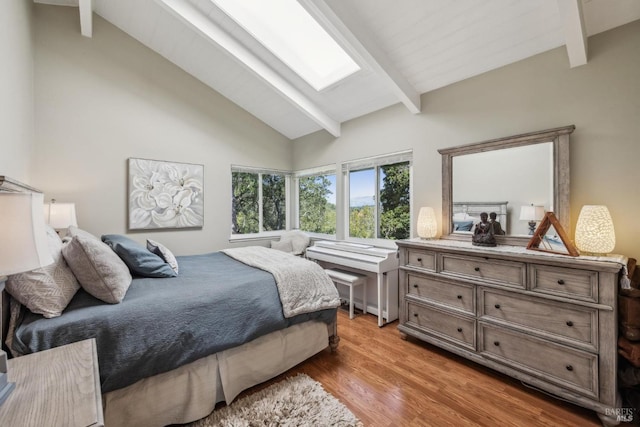bedroom featuring beam ceiling, high vaulted ceiling, light wood-style flooring, and a skylight