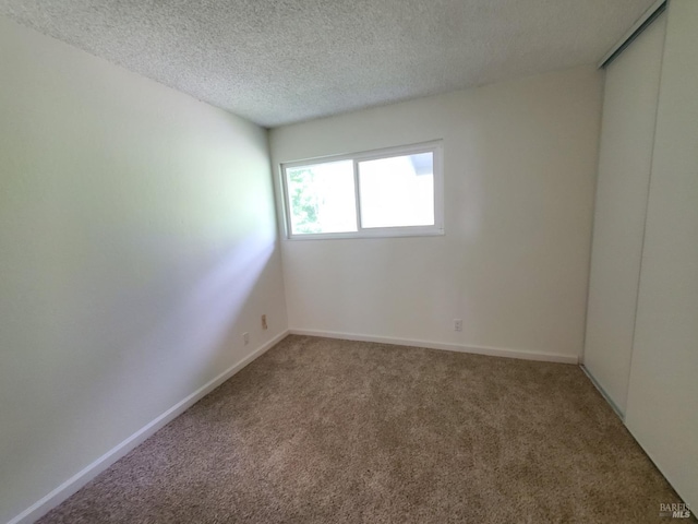 carpeted empty room with a textured ceiling and baseboards
