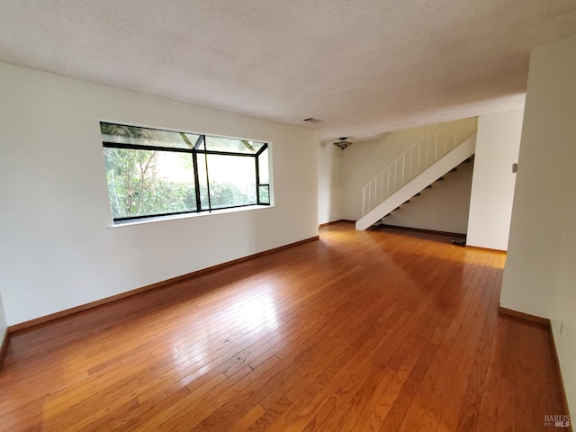unfurnished room with visible vents, hardwood / wood-style floors, stairway, and baseboards