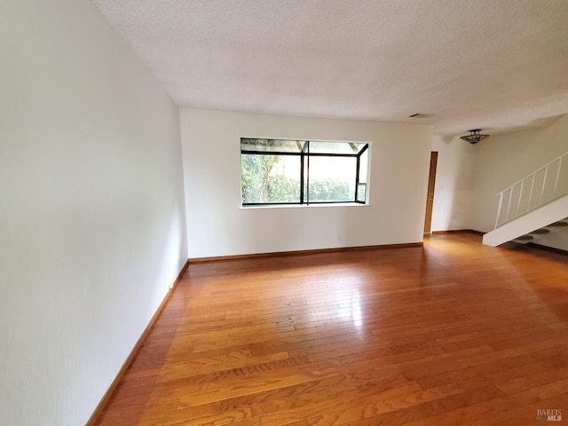spare room with stairs, baseboards, a textured ceiling, and light wood-style floors