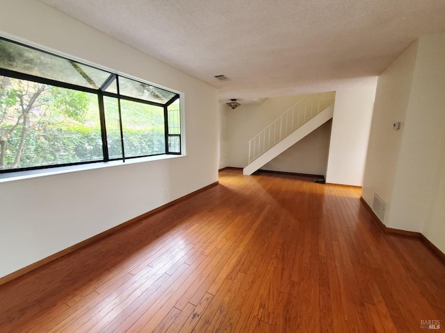 spare room featuring baseboards, visible vents, hardwood / wood-style flooring, and stairway