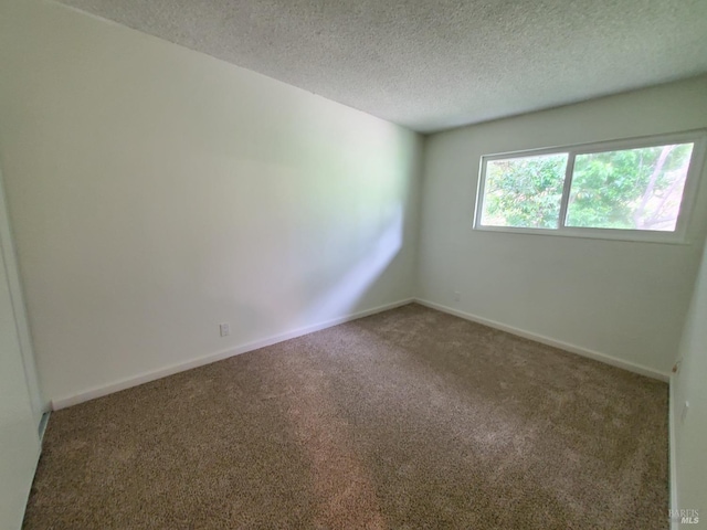 carpeted spare room featuring a textured ceiling and baseboards