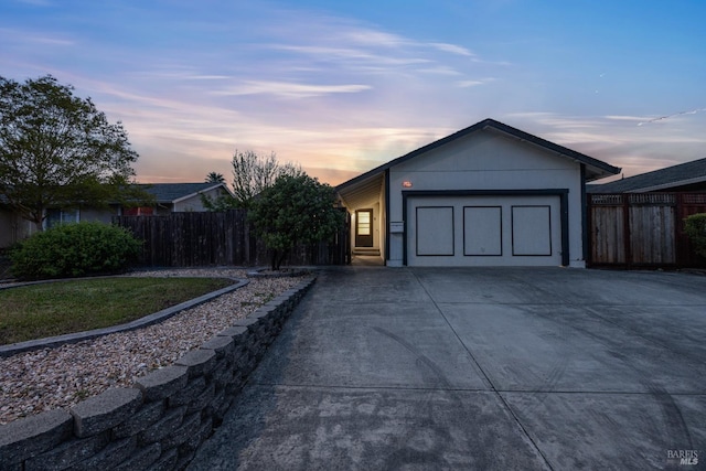 garage at dusk featuring fence and driveway