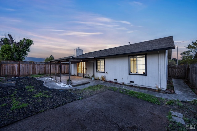 back of property at dusk featuring a chimney, a fenced backyard, a shingled roof, a patio, and crawl space
