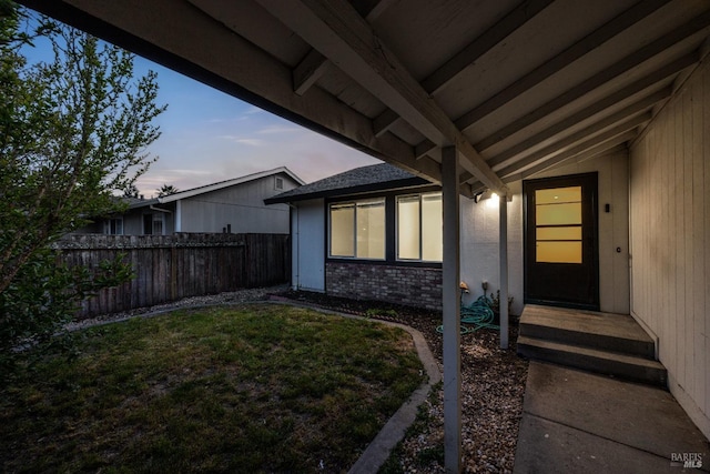 exterior entry at dusk with a lawn and fence