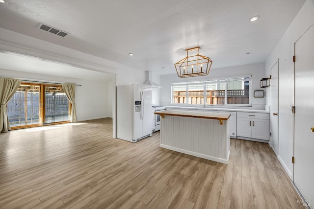 kitchen with white appliances, an inviting chandelier, light wood-style flooring, wall chimney range hood, and visible vents