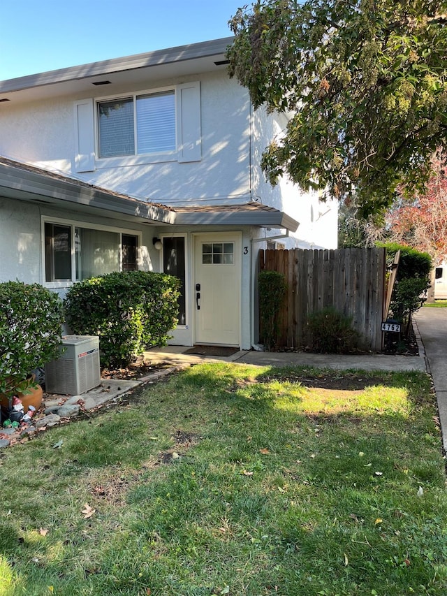 traditional home featuring stucco siding, fence, central AC, and a front lawn