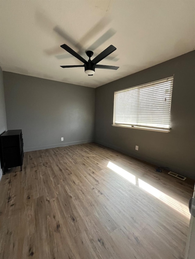 unfurnished room with a ceiling fan, visible vents, wood finished floors, and baseboards
