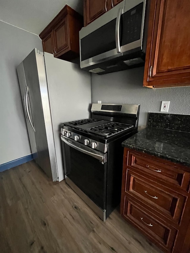 kitchen featuring baseboards, stainless steel appliances, dark wood-type flooring, and dark stone counters