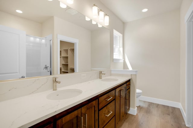 bathroom with a shower with shower door, double vanity, a sink, and wood finished floors