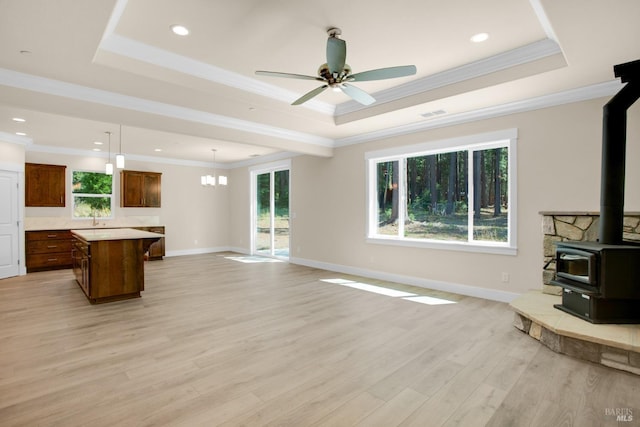 unfurnished living room featuring a wood stove, a sink, a tray ceiling, light wood-type flooring, and a ceiling fan