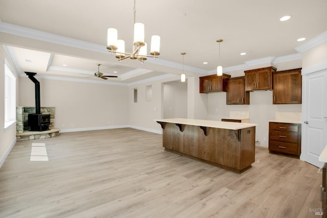 kitchen featuring a wood stove, light wood-style floors, a kitchen breakfast bar, a center island, and ceiling fan with notable chandelier