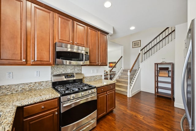 kitchen with light stone countertops, dark wood-style flooring, appliances with stainless steel finishes, and baseboards