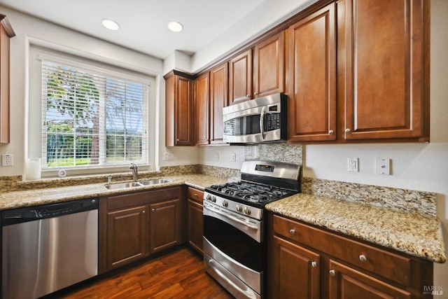 kitchen featuring light stone countertops, recessed lighting, stainless steel appliances, a sink, and dark wood-style floors