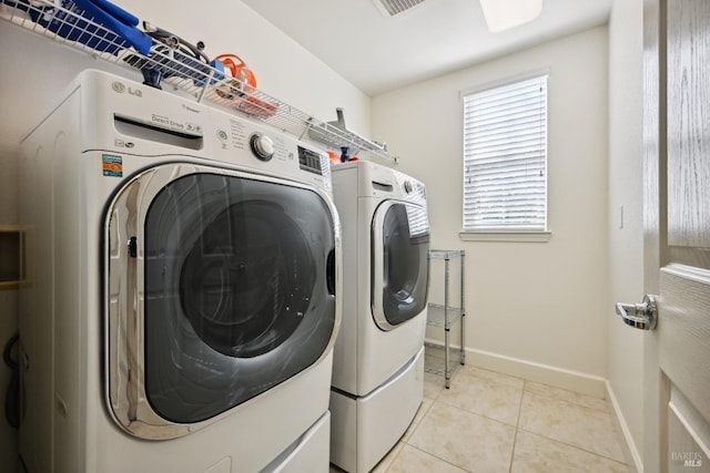 clothes washing area with baseboards, light tile patterned floors, washing machine and clothes dryer, and laundry area