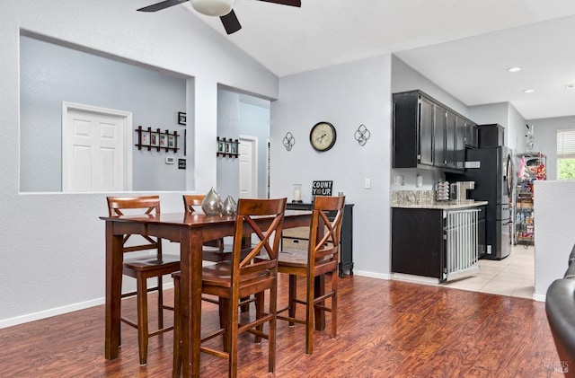 dining room with a ceiling fan, a bar, lofted ceiling, and light wood-type flooring