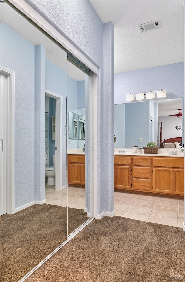 bathroom featuring carpet, toilet, a textured wall, vanity, and visible vents