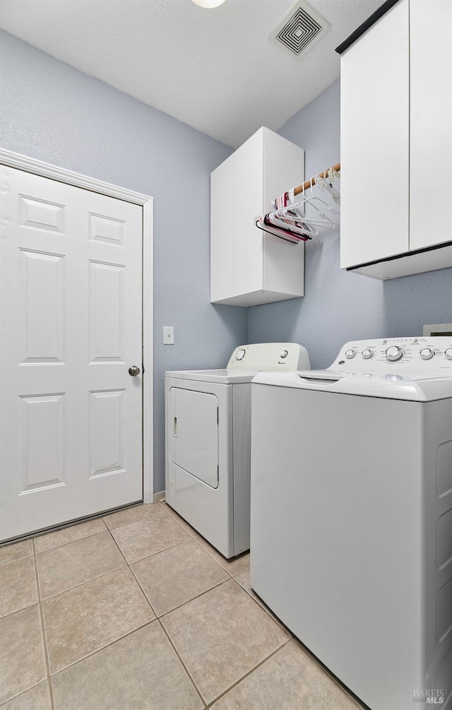 clothes washing area featuring light tile patterned floors, cabinet space, independent washer and dryer, and visible vents