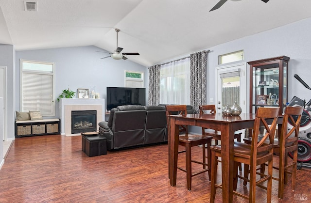 dining area featuring a fireplace, ceiling fan, visible vents, vaulted ceiling, and dark wood finished floors