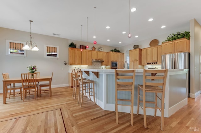 kitchen with built in microwave, baseboards, light wood-type flooring, under cabinet range hood, and visible vents