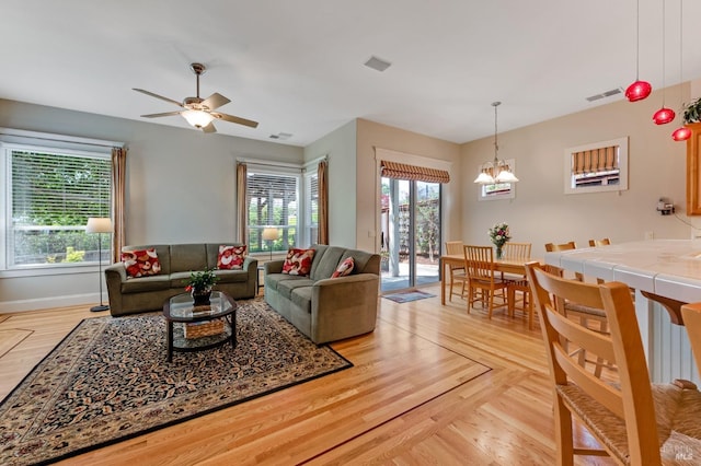 living area with baseboards, visible vents, light wood-style flooring, and ceiling fan with notable chandelier