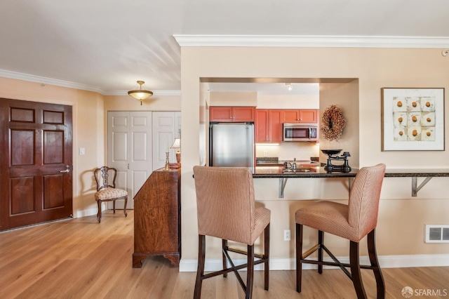 1483 Sutter St Unit 901, San Francisco, CA 94109 - kitchen featuring appliances with stainless steel finishes, a kitchen bar, dark countertops, crown molding, and light wood-style flooring