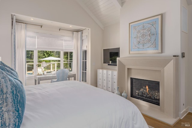 bedroom with a warm lit fireplace, wood finished floors, and vaulted ceiling