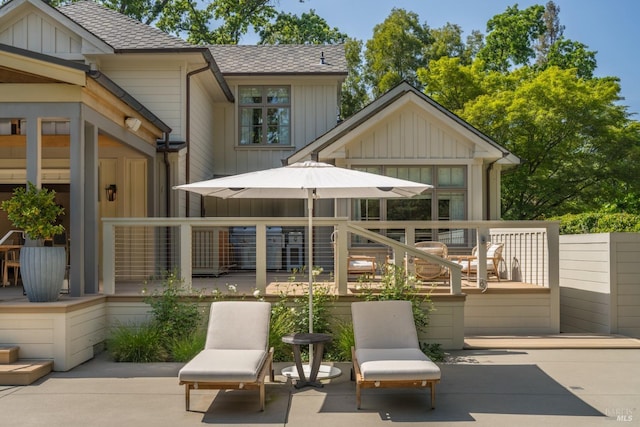 rear view of house with a shingled roof, a patio, board and batten siding, and a deck