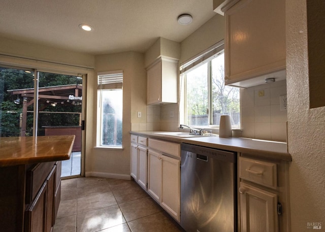 kitchen with tasteful backsplash, stainless steel dishwasher, white cabinets, a sink, and light tile patterned flooring