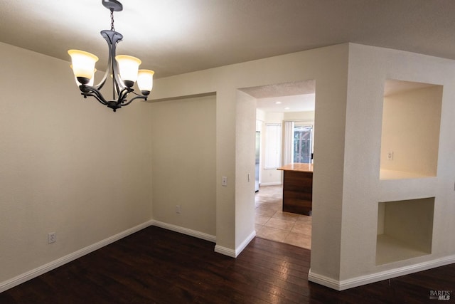 empty room featuring wood-type flooring, an inviting chandelier, and baseboards