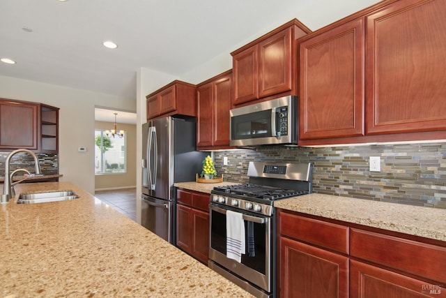 kitchen featuring light stone countertops, decorative backsplash, a chandelier, appliances with stainless steel finishes, and a sink
