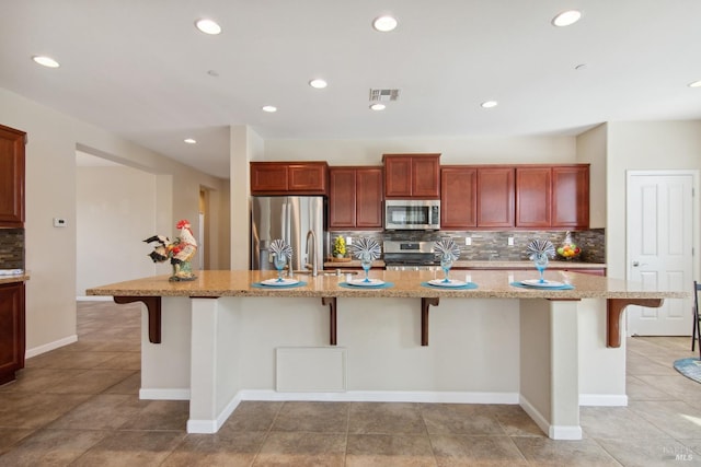 kitchen with light stone counters, a kitchen breakfast bar, decorative backsplash, appliances with stainless steel finishes, and visible vents