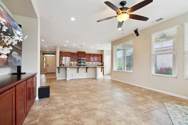 unfurnished living room with light tile patterned floors, visible vents, ceiling fan, and baseboards