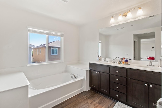 bathroom featuring double vanity, wood finished floors, a garden tub, and a sink
