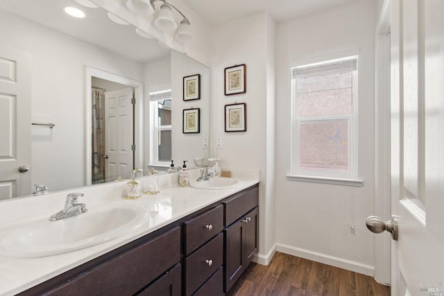 full bathroom with baseboards, wood finished floors, double vanity, and a sink
