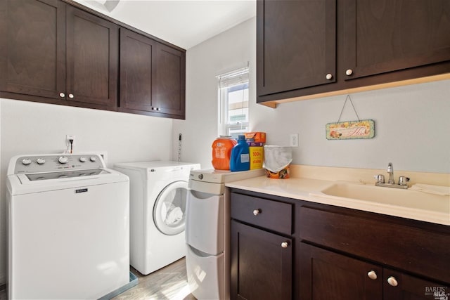 washroom featuring light wood-type flooring, cabinet space, washer and clothes dryer, and a sink