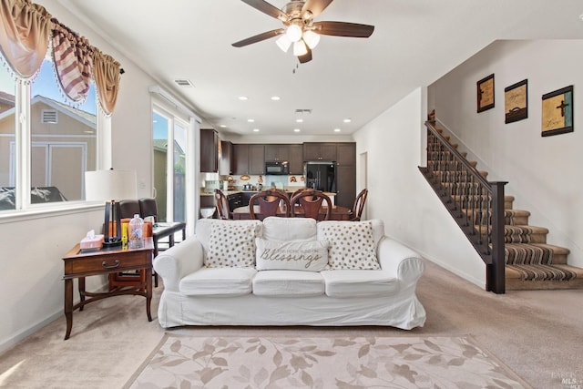 living room featuring stairs, light colored carpet, baseboards, visible vents, and a ceiling fan