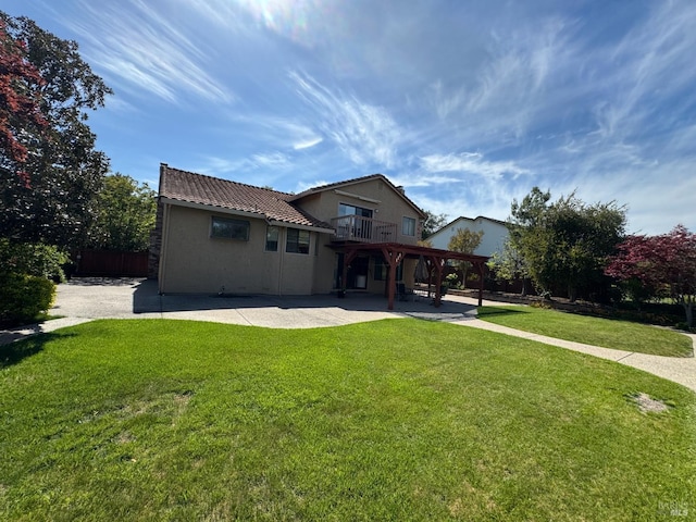 rear view of property featuring a balcony, a tile roof, a patio area, stucco siding, and a lawn