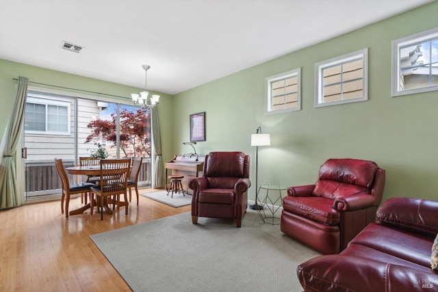 living room with an inviting chandelier, light wood-style flooring, and visible vents