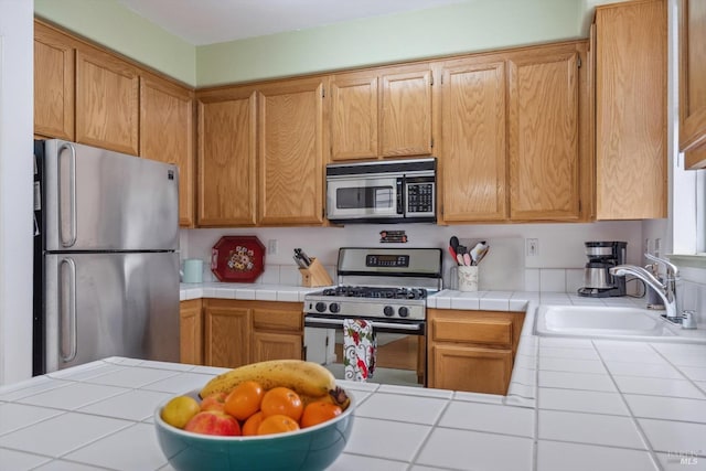 kitchen with a sink, tile counters, and stainless steel appliances