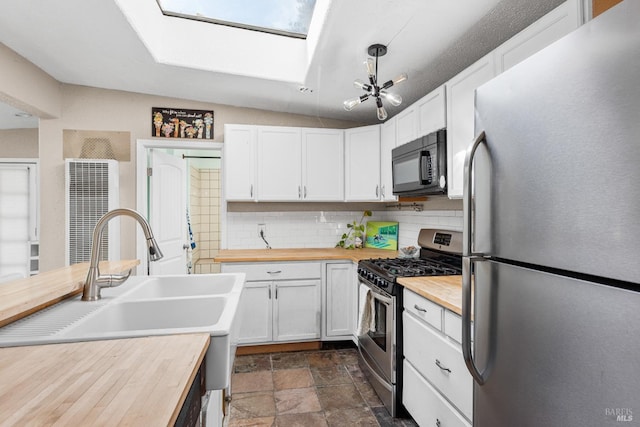 kitchen featuring a heating unit, butcher block countertops, stainless steel appliances, backsplash, and a skylight