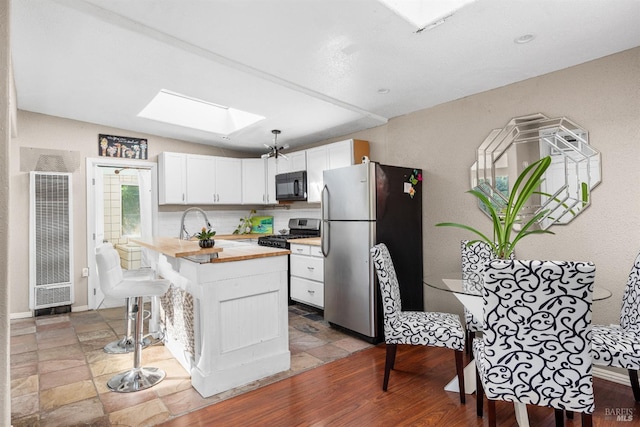 kitchen with a skylight, appliances with stainless steel finishes, wood counters, white cabinetry, and a heating unit